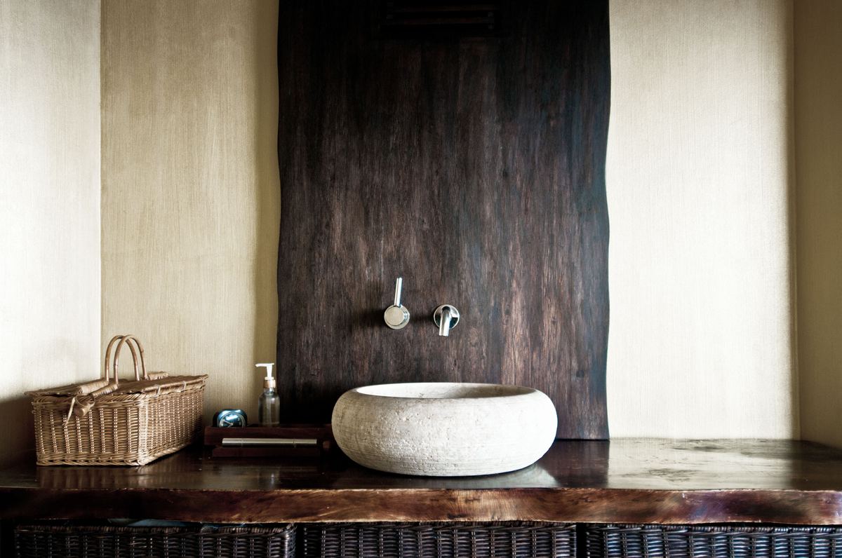Baño con lavabo de piedra sobre encimera de madera oscura y pared de estuco