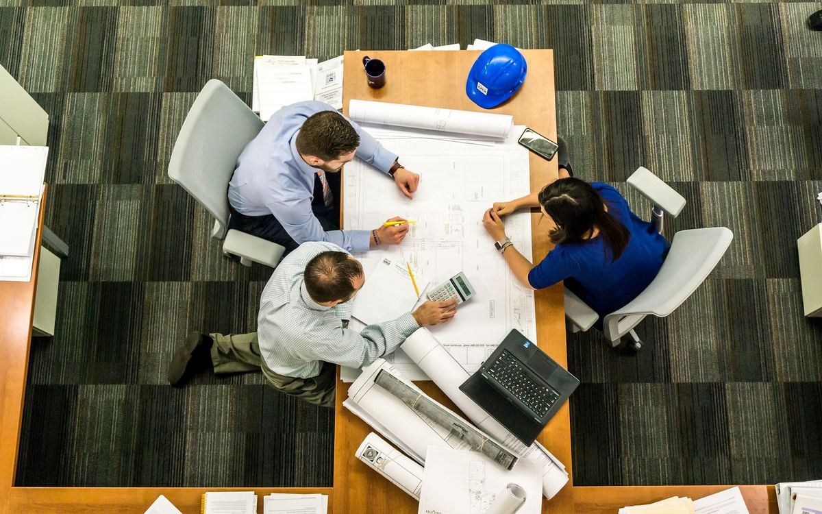 Tres personas revisan planos y un casco de obra sobre una mesa