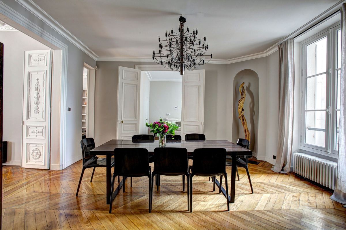 Comedor con parquet en espiga, mesa negra y puertas acristaladas